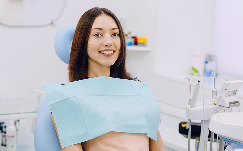 A woman wearing a face mask is sitting in a dental chair with her mouth open for a dental examination.