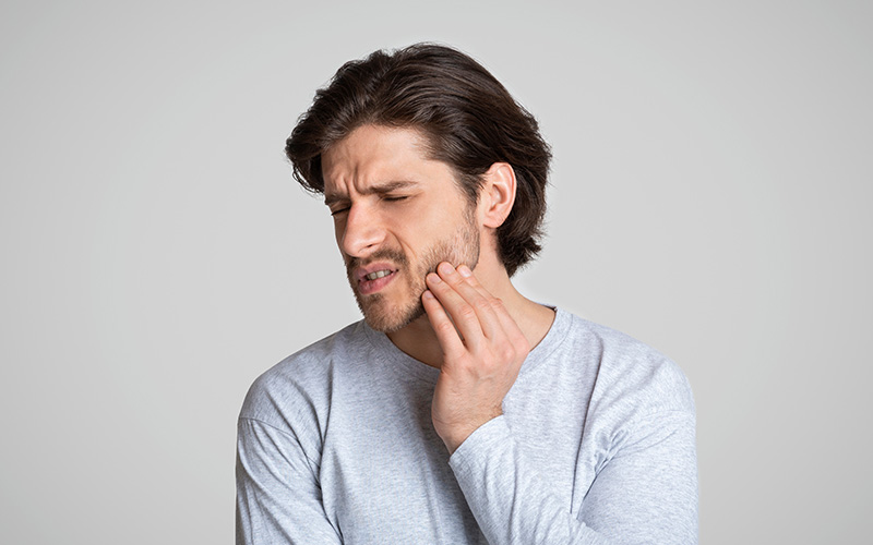 The image shows a man with facial hair looking distressed and holding his nose, suggesting he might be experiencing discomfort or pain.